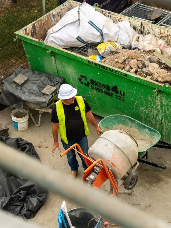 Labourer moving a concrete mixer beside a skip bin